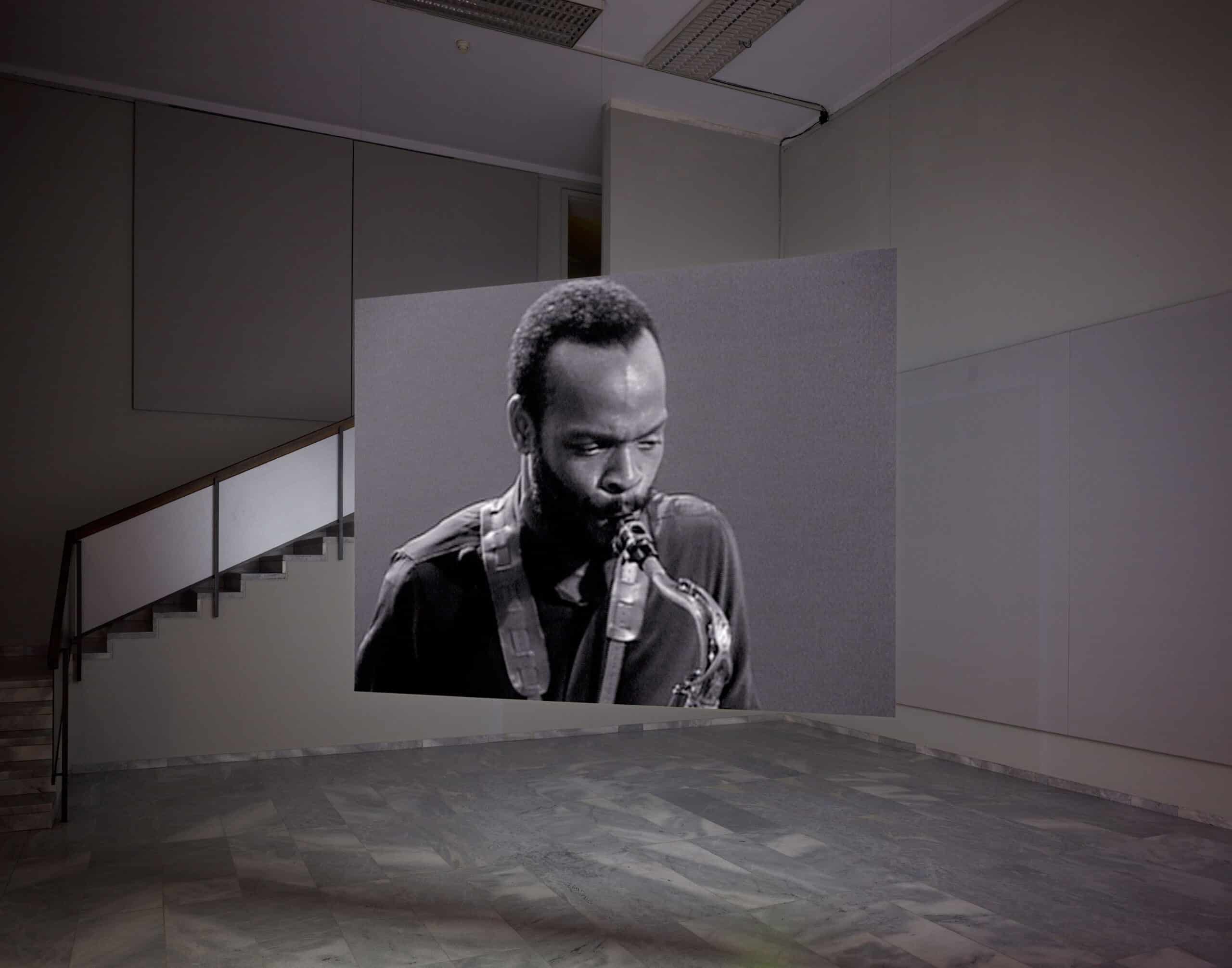 Vue de l’installation Hors-champs de Stan Douglas, avec un musicien projeté sur un écran suspendu